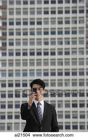 Picture - Businessman looking through camera phone. Fotosearch