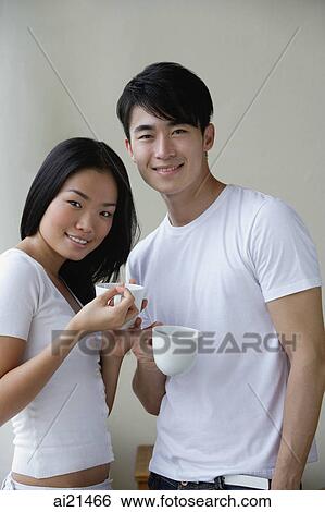 Couple holding cups, smiling at camera View Large Photo Image Stock Photograph - Couple holding cups, smiling at camera. Fotosearch