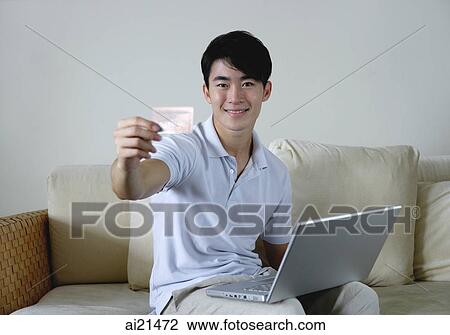 Man sitting on sofa with laptop, holding out credit card View Large Photo Image Stock Image - Man sitting on sofa with laptop, holding out credit card. Fotosearch