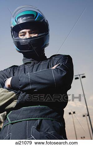Stock Photo - Race car driver in protective sportswear, arms crossed, looking at camera. Fotosearch