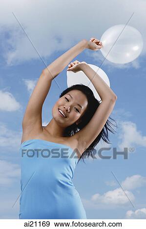 Woman holding balloons in air, smiling at camera View Large Photo Image Stock Photo - Woman holding balloons in air, smiling at camera. Fotosearch