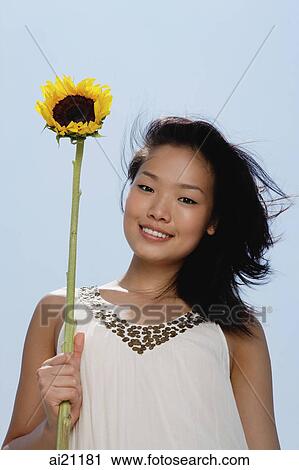 Woman holding sunflower stalk, smiling at camera View Large Photo Image Stock Image - Woman holding sunflower stalk, smiling at camera. Fotosearch