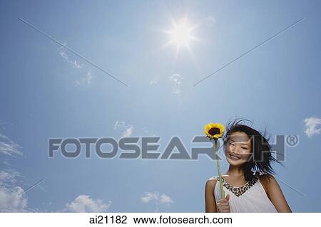 Woman holding sunflower stalk, smiling at camera, low angle view View Large Photo Image Stock Image - Woman holding sunflower stalk, smiling at camera, low angle view. Fotosearch