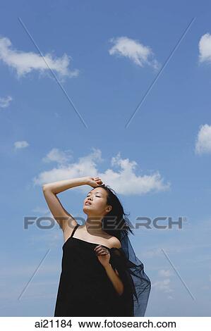 Picture - Woman in black dress, hand on head, eyes closed, head tilted back. Fotosearch