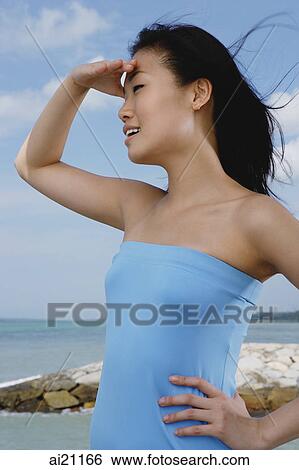 Stock Photograph - Woman in blue tube top, shielding eyes, looking away. Fotosearch