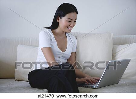 Woman sitting on sofa, using laptop View Large Photo Image Stock Image - Woman sitting on sofa, using laptop. Fotosearch