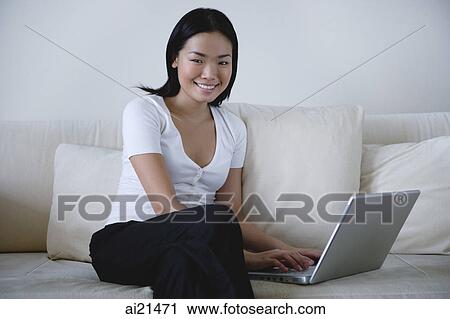 Woman sitting on sofa, using laptop, smiling at camera View Large Photo Image Stock Image - Woman sitting on sofa, using laptop, smiling at camera. Fotosearch