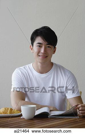 Young man having breakfast and reading a magazine, smiling at camera View Large Photo Image Picture - Young man having breakfast and reading a magazine, smiling at camera. Fotosearch