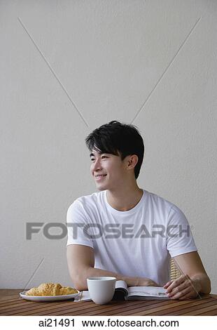Young man having breakfast and reading a magazine View Large Photo Image Stock Image - Young man having breakfast and reading a magazine. Fotosearch