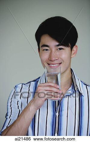 Young man holding glass of water, smiling View Large Photo Image Stock Photograph - Young man holding glass of water, smiling. Fotosearch