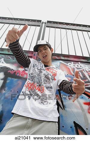 Young man in front of graffiti covered wall, making hand sign View Large Photo Image Stock Image - Young man in front of graffiti covered wall, making hand sign. Fotosearch