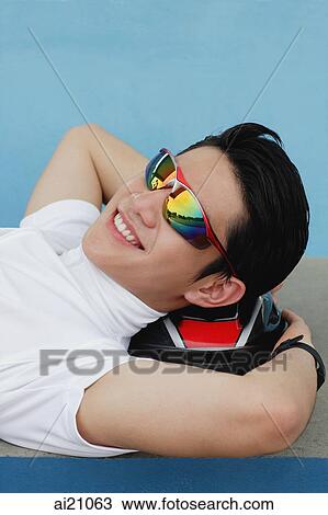 Young man lying on cycling helmet, wearing sunglasses, smiling View Large Photo Image Stock Image - Young man lying on cycling helmet, wearing sunglasses, smiling. Fotosearch