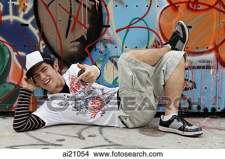 Young man lying on floor, next to graffiti covered wall, making hand sign View Large Photo Image Picture - Young man lying on floor, next to graffiti covered wall, making hand sign. Fotosearch