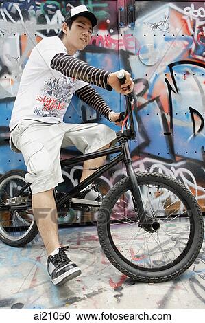 Stock Image - Young man on bicycle in front of graffiti wall. Fotosearch