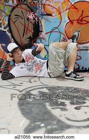Young man reclining next to graffiti covered wall, making hand sign View Large Photo Image Stock Photography - Young man reclining next to graffiti covered wall, making hand sign. Fotosearch