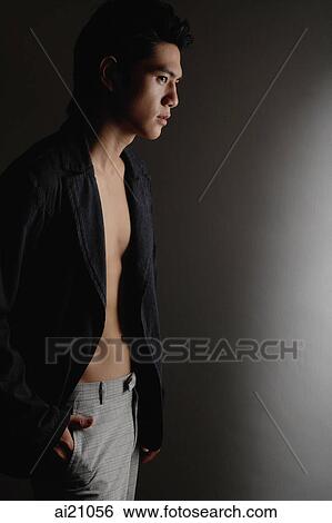 Young man standing against dark background View Large Photo Image Stock Photograph - Young man standing against dark background. Fotosearch