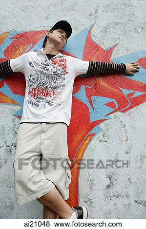 Young man standing against graffiti wall, arms outstretched View Large Photo Image Stock Photo - Young man standing against graffiti wall, arms outstretched. Fotosearch