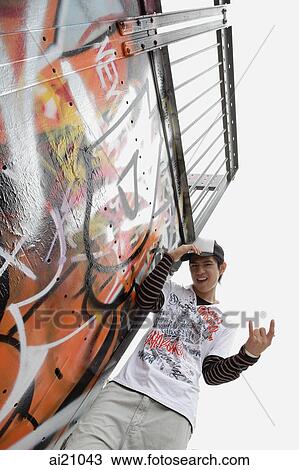 Young man standing next to graffiti covered wall, looking at camera View Large Photo Image Stock Image - Young man standing next to graffiti covered wall, looking at camera. Fotosearch
