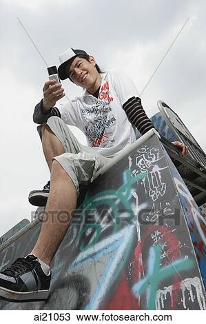 Young man text messaging, sitting on graffiti covered ledge View Large Photo Image Stock Image - Young man text messaging, sitting on graffiti covered ledge. Fotosearch