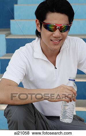 Young man wearing sunglasses, holding bottled water View Large Photo Image Stock Photo - Young man wearing sunglasses, holding bottled water. Fotosearch