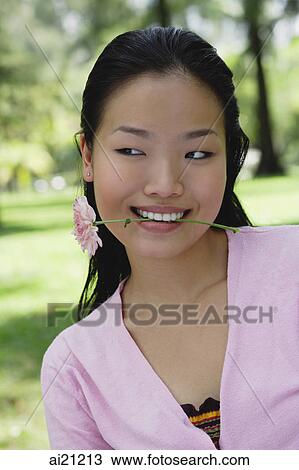 Young woman biting flower stalk, head shot View Large Photo Image Stock Image - Young woman biting flower stalk, head shot. Fotosearch