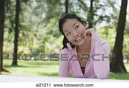 Young woman biting flower stalk, sitting outdoors View Large Photo Image Stock Image - Young woman biting flower stalk, sitting outdoors. Fotosearch