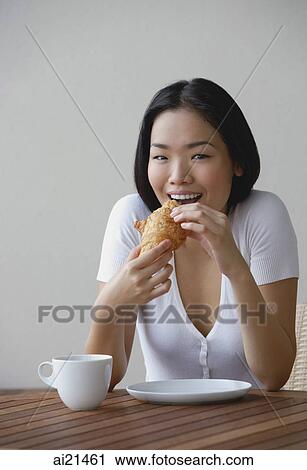 Stock Image - Young woman eating a croissant. Fotosearch
