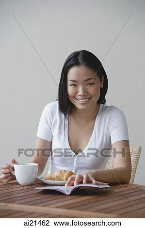 Young woman having breakfast and reading a book, smiling at camera View Large Photo Image Stock Image - Young woman having breakfast and reading a book, smiling at camera. Fotosearch