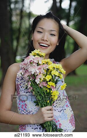 Young woman holding bouquet of flowers, hand on head, smiling at camera View Large Photo Image Stock Image - Young woman holding bouquet of flowers, hand on head, smiling at camera. Fotosearch