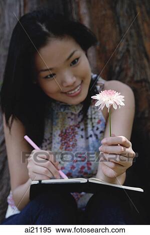 Young woman holding flower, writing in notebook View Large Photo Image Stock Photography - Young woman holding flower, writing in notebook. Fotosearch