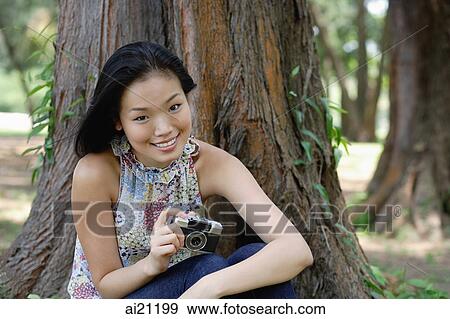 Stock Photo - Young woman outdoors, holding a camera, smiling. Fotosearch