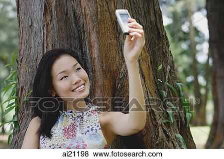 Young woman outdoors, taking a photograph of herself with mobile phone camera View Large Photo Image Stock Photo - Young woman outdoors, taking a photograph of herself with mobile phone camera. Fotosearch