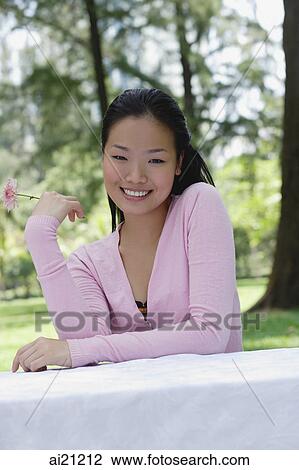 Young woman sitting at outdoor table, holding single flower stalk View Large Photo Image Stock Image - Young woman sitting at outdoor table, holding single flower stalk. Fotosearch
