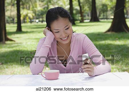 Young woman sitting at outdoor table, listening to MP3 player View Large Photo Image Stock Photograph - Young woman sitting at outdoor table, listening to MP3 player. Fotosearch