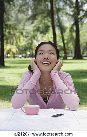 Stock Photo - Young woman sitting outdoors, listening to MP3 player. Fotosearch