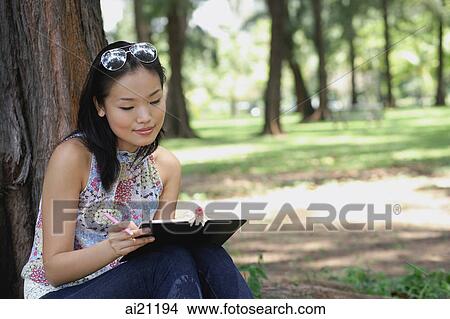 Young woman sitting outdoors, writing in notebook View Large Photo Image Picture - Young woman sitting outdoors, writing in notebook. Fotosearch