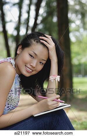 Stock Photo - Young woman with flower and notebook, hand on head, smiling at camera. Fotosearch