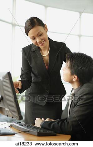 Stock Image - Businessman and businesswoman having a discussion, desktop computer on table in front of them. Fotosearch