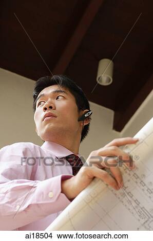Businessman holding blueprints, using hands free device, looking away View Large Photo Image Picture - Businessman holding blueprints, using hands free device, looking away. Fotosearch