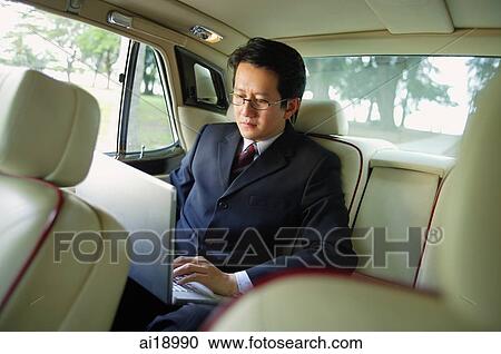 Stock Image - Businessman in car, using laptop. Fotosearch