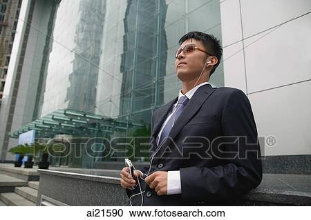 Stock Image - Businessman in city location, listening to MP3 player. Fotosearch
