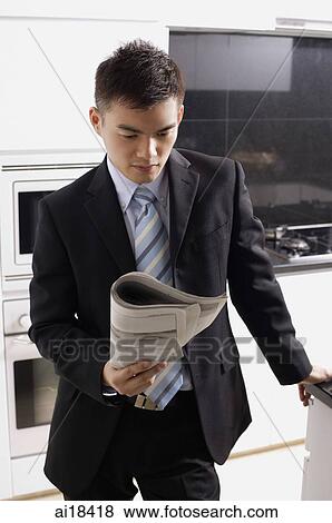Businessman in kitchen, looking at newspaper View Large Photo Image Stock Photo - Businessman in kitchen, looking at newspaper. Fotosearch
