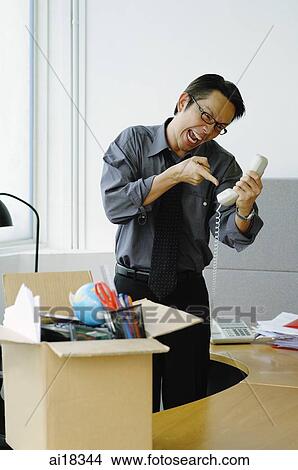 Businessman in office, shouting and pointing at telephone receiver, box full of items on top of desk View Large Photo Image Picture - Businessman in office, shouting and pointing at telephone receiver, box full of items on top of desk. Fotosearch