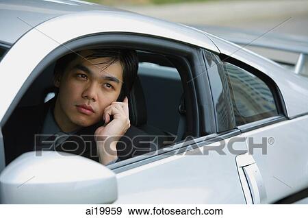 Stock Photo - Businessman in silver sports car, using mobile phone. Fotosearch