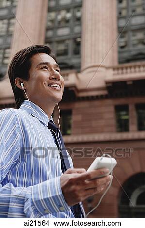 Businessman in the city, listening to MP3 player View Large Photo Image Picture - Businessman in the city, listening to MP3 player. Fotosearch