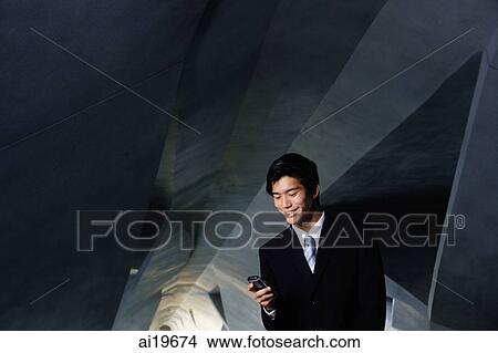Picture - Businessman in tunnel, looking at mobile phone. Fotosearch