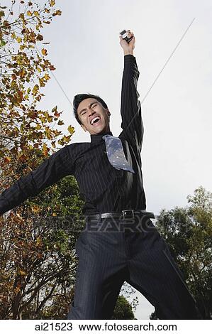 Stock Image - Businessman jumping in air, arm raised in victory. Fotosearch