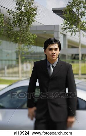 Businessman leaning on car, looking at camera View Large Photo Image Picture - Businessman leaning on car, looking at camera. Fotosearch