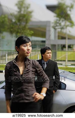 Businessman leaning on car, woman in foreground, with hand on hip View Large Photo Image Stock Photography - Businessman leaning on car, woman in foreground, with hand on hip. Fotosearch