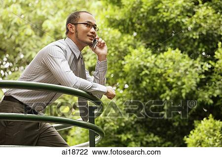 Businessman leaning on railing, using mobile phone View Large Photo Image Stock Image - Businessman leaning on railing, using mobile phone. Fotosearch